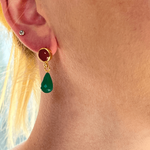 A close up of the ear and neck of a white woman with blonde hair, wearing an earring with a teardrop shaped green stone.